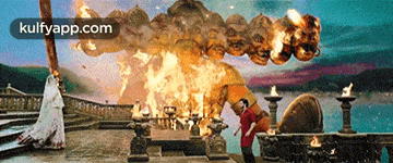 a man is standing on a balcony looking at a large explosion with the website kulfyapp.com visible in the corner