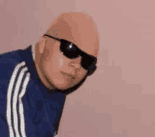 a bald man wearing sunglasses and a fake head is looking at the camera .