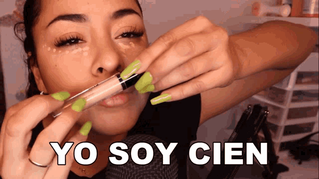 a woman with green nails is applying concealer to her face and the words yo soy cien are above her