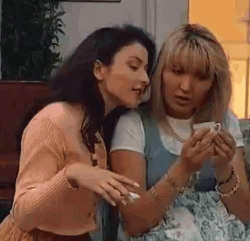 two women are sitting on a couch looking at a cell phone together .