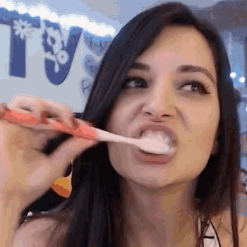 a woman is brushing her teeth with a toothbrush and making a funny face .
