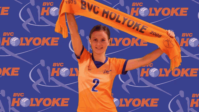 a woman holding up an orange scarf that says bvc holyoke