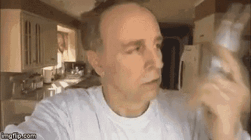 a man is taking a selfie in a kitchen while holding a bottle of water .