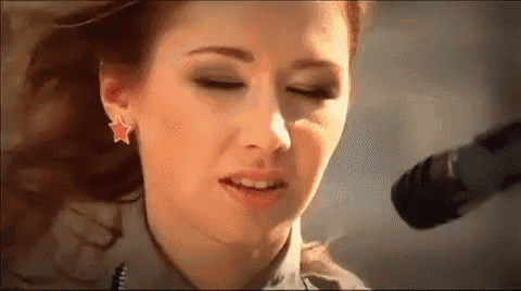 a woman is singing into a microphone while wearing earrings with a star on them .