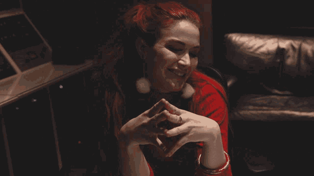 a woman with red hair is smiling with her hands folded in front of her face