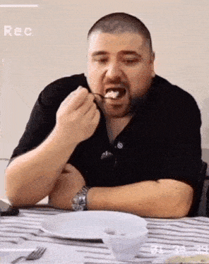 a man is sitting at a table with a plate of food and a watch on his wrist while eating food