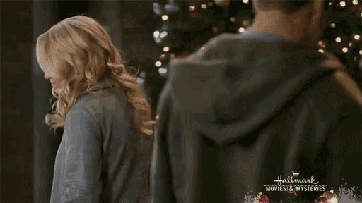 a woman in a grey coat says bye chris in front of a christmas tree