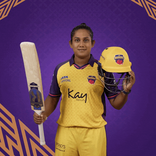 a female cricket player holding a bat and a helmet that says warriors
