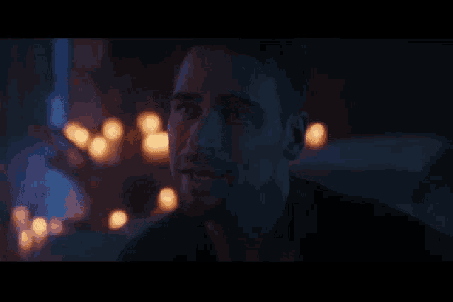 a close up of a man 's face in a dark room with candles in the background .