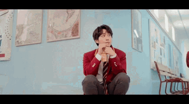 a young man in a red jacket and tie is sitting on the floor in a hallway looking up .