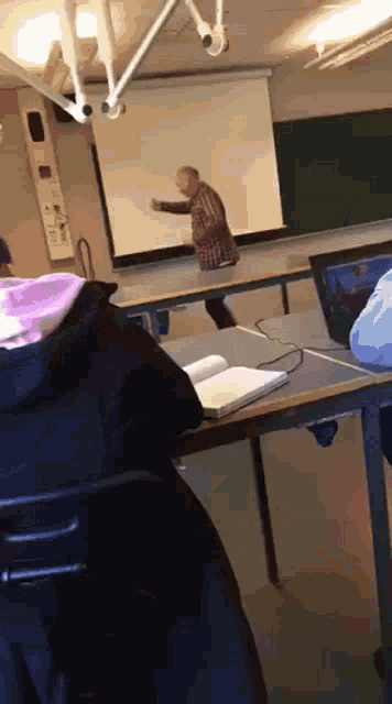 a man in a plaid shirt stands in front of a projector screen in a classroom