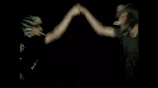 a group of people are dancing in a dark room and one of them is wearing a hat .