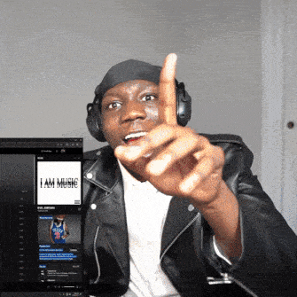 a man wearing headphones and a leather jacket points at a screen that says i am music