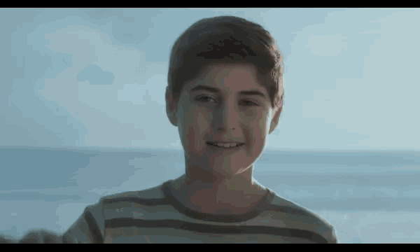 a young boy is smiling and looking at the camera while standing on the beach .