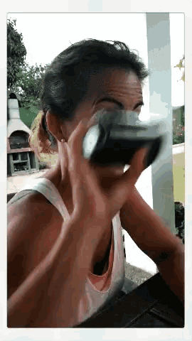 a woman is drinking from a bottle while sitting on a porch