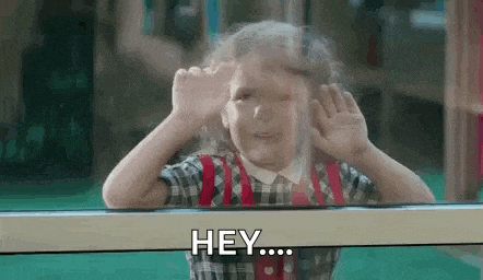 a little girl is looking out of a window with her hands up and saying `` hey '' .