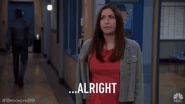 a woman in a red shirt is standing in a hallway and says alright