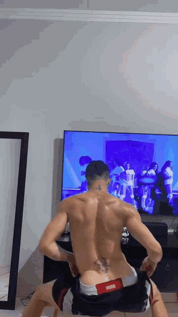 a man without a shirt is squatting in front of a tv .