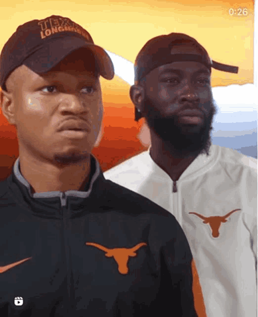 a man wearing a texas longhorn hat stands next to another man wearing a nike jacket