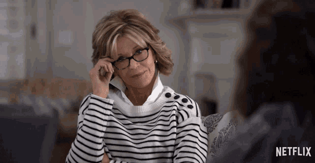 a woman wearing glasses and a striped sweater is sitting on a couch in front of a netflix logo
