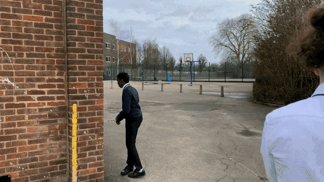 a man standing in front of a brick wall with a basketball court behind him