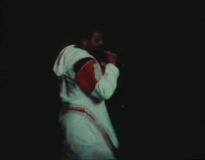 a man in a white and red jacket is singing into a microphone in the dark