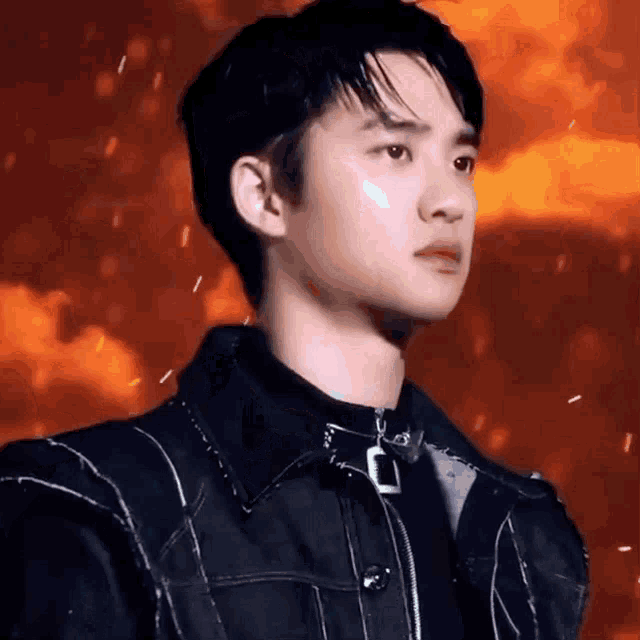 a close up of a young man wearing a black jacket and a black shirt with fire in the background .
