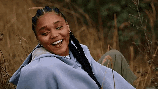 a woman in a blue hoodie is smiling while sitting in the grass .