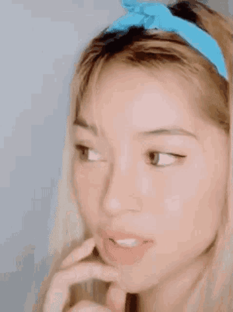 a close up of a woman wearing a blue headband covering her face with her hand .