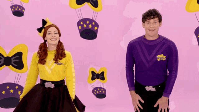 a man and a woman are standing in front of a pink background with wiggle balloons