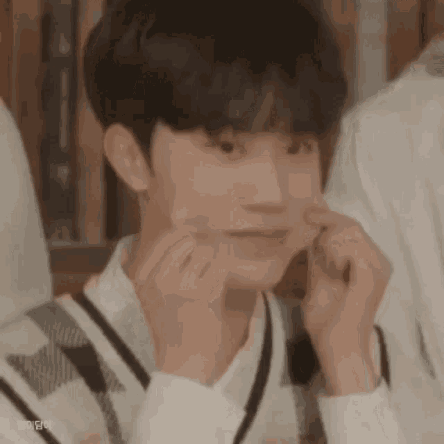 a young man is making a funny face with his hands while sitting in front of a bookshelf .