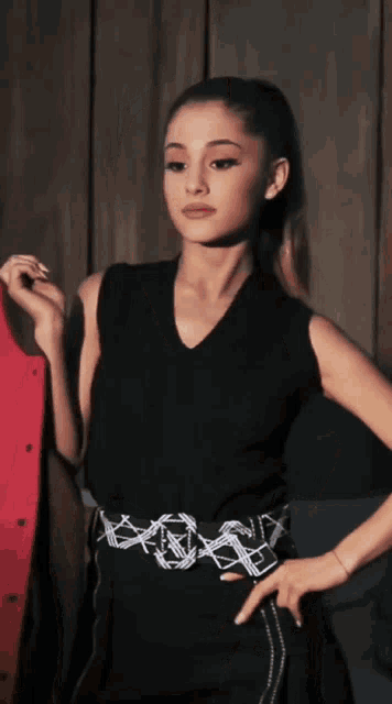 a woman wearing a black top and a white belt has her hands on her hip