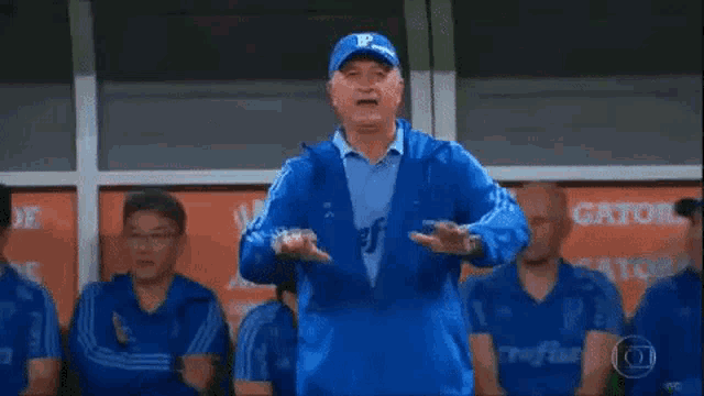 a man in a blue jacket and hat is standing in front of a group of men in blue uniforms .