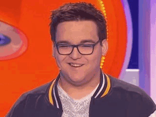 a young man wearing glasses and a varsity jacket is smiling .