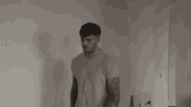 a man with tattoos on his arms is standing in front of a mirror in a living room .