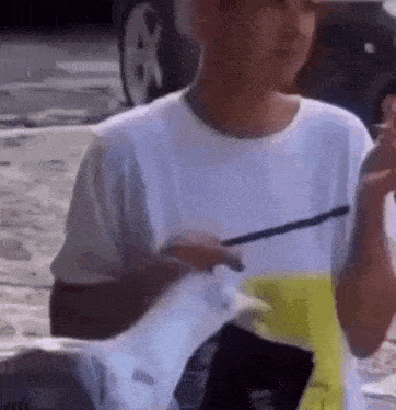 a man in a white t-shirt is holding a piece of paper and a cigarette .