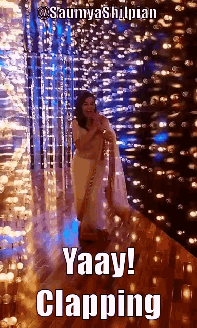 a woman in a white dress is clapping in front of a wall of lights