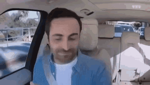 a man in a blue shirt is sitting in a car with his eyes closed .