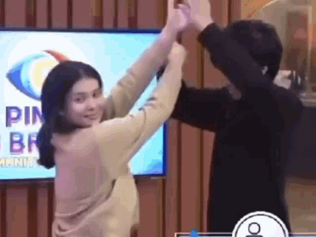 a man and a woman are giving each other a high five in front of a tv .
