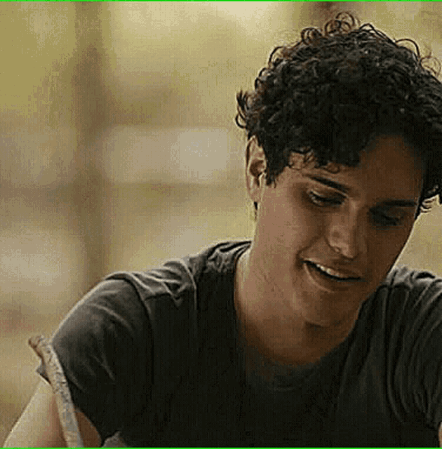 a young man with curly hair is smiling and wearing a black shirt