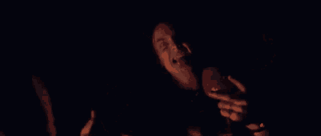 a man is smoking a cigarette in the dark while wearing a black shirt .