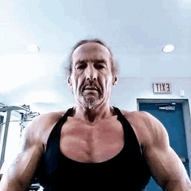 a man with a beard is flexing his muscles in a gym and looking at the camera .