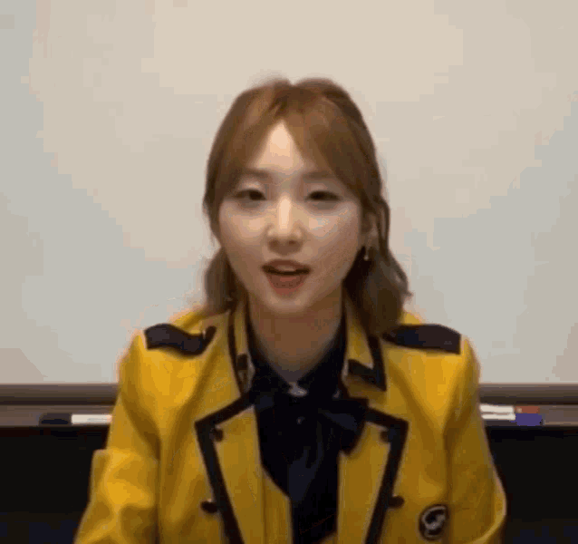 a young woman in a yellow school uniform is sitting in front of a whiteboard .