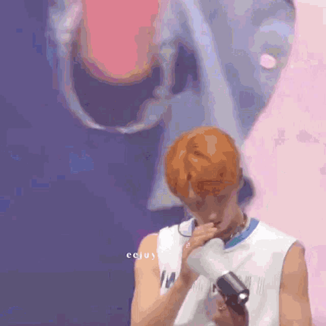 a man with red hair is holding a microphone in front of a wall that says ' eeeju ' on it