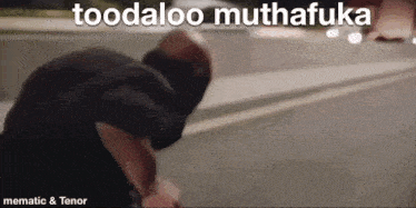 a man is standing on the side of the road with the words toodaloo muthafuka above him .