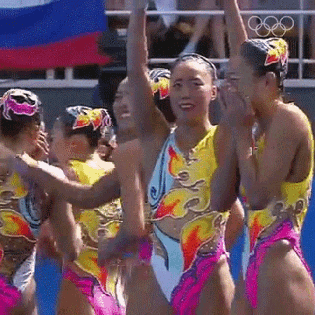 a group of synchronized swimmers are celebrating their victory with their arms in the air .