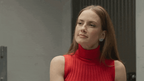 a woman wearing a red sweater and earrings is looking at the camera and smiling .