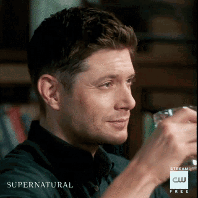 a man in a black shirt is drinking from a glass with the words supernatural on the bottom