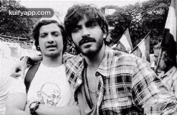 a black and white photo of two men standing next to each other . one of the men is wearing a plaid shirt .