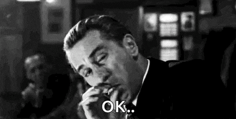 a man in a suit and tie is smoking a cigarette and saying ok .